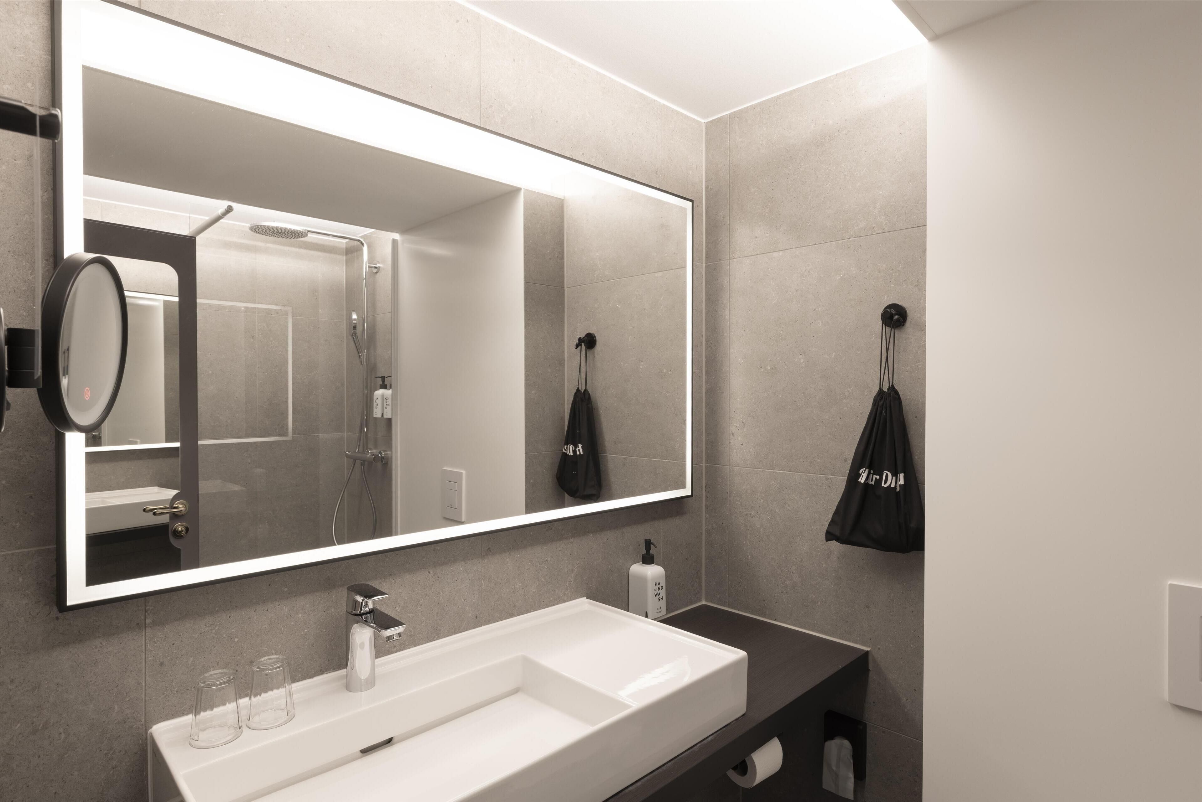 Un baño moderno con un espejo grande, un lavabo blanco y una zona de ducha.
