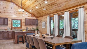 A wooden cabin with a dining area, kitchen, and large windows. - Indoor Pool, Theater, Game Room • 10mins to Pigeon Forge | Bluebell by AvantStay (Sevierville)
