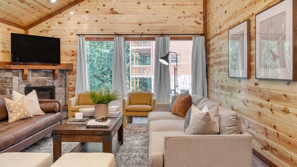 A cozy log cabin interior with a stone fireplace, leather sofas, a coffee table, and a television mounted on the wall. - Indoor Pool, Theater, Game Room • 10mins to Pigeon Forge | Bluebell by AvantStay (Sevierville)