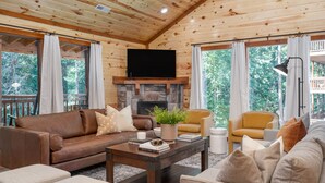 A cozy cabin interior with a stone fireplace, leather sofas, and a television. - Indoor Pool, Theater, Game Room • 10mins to Pigeon Forge | Bluebell by AvantStay (Sevierville)