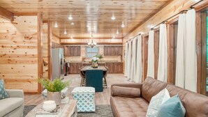 Interior de cabana de tronco com sala de estar, cozinha e área de jantar.
