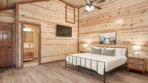 Quarto com painéis de madeira, cama, abajures, ventoinha de teto e TV na parede.