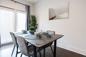 A dining area with a table set for four, surrounded by chairs. There is a potted plant on the table, and a painting on the wall.