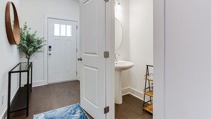 A hallway with a white door, a glass table with a plant, a round mirror, a white sink, and a black shelf with a plant. - ❤ of Stonecrest☀1556ft²☀Backyard☀Parking☀W/D (stone crest)