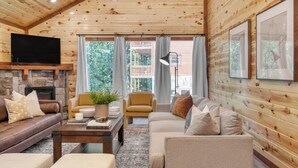 A cozy log cabin interior with a stone fireplace, leather sofas, a coffee table, and a television mounted on the wall. - Bluestem & Bluebell by AvantStay | Incredible Views w/ Balcony & Indoor Pool! (Sevierville)