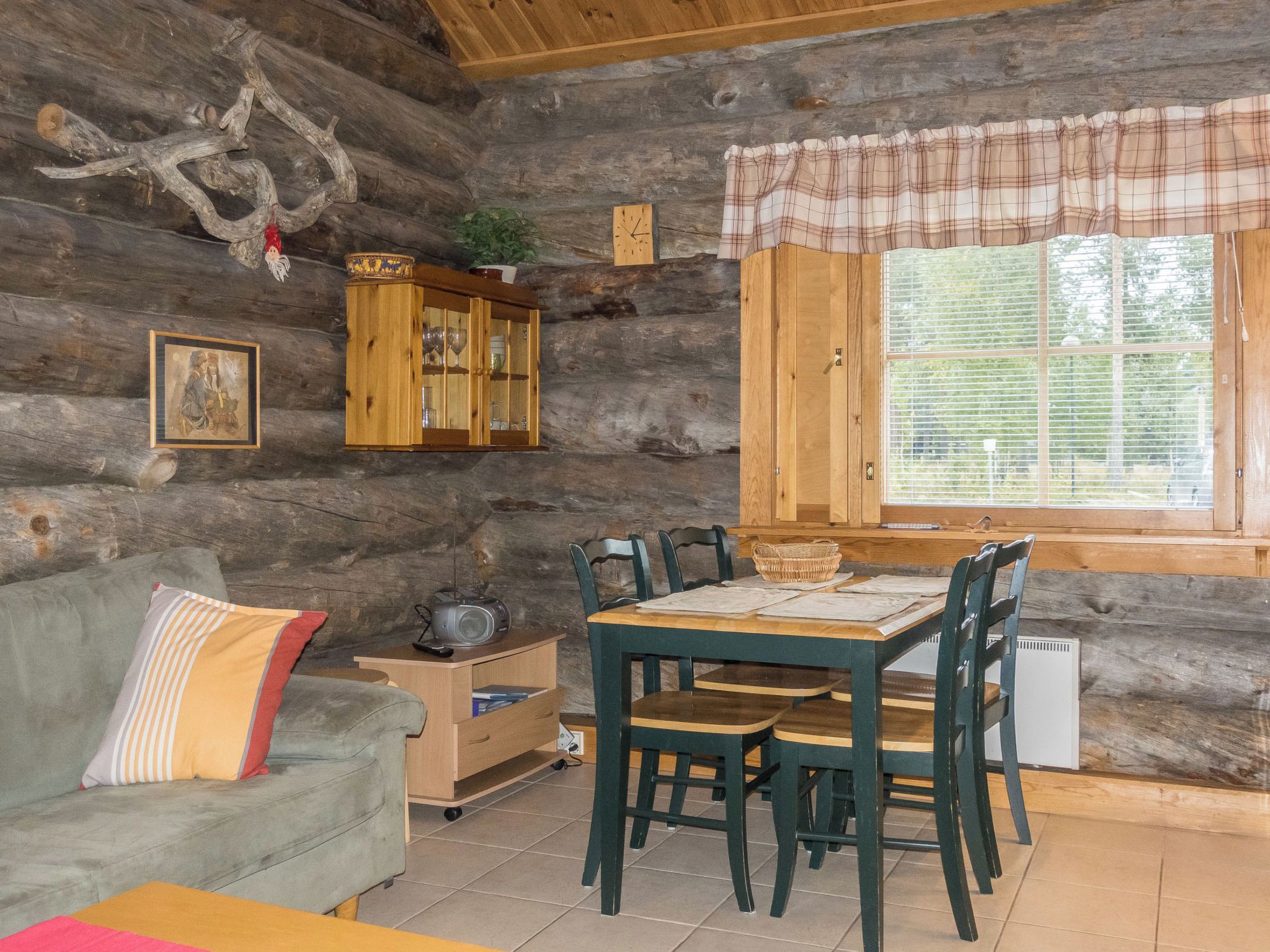 Interior rústico de una cabaña con una mesa de comedor de madera, sillas, un sofá, un armario y una ventana con persianas.