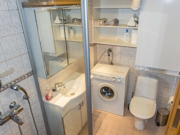 A compact bathroom with a shower, sink, washing machine, toilet, and a mirror. - Lauri 2 by Interhome (Kittilä)