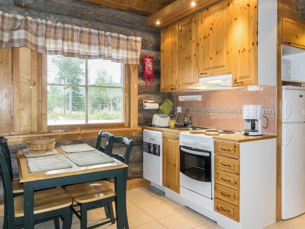 A kitchen with wooden cabinets, a dining table with chairs, and a window with blinds. - Lauri 2 by Interhome (Kittilä)
