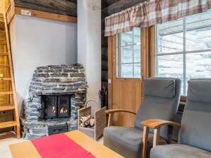 A cozy room with a stone fireplace, wooden furniture, and a window with blinds. - Lauri 2 by Interhome (Kittilä)