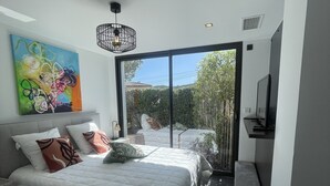 Un dormitorio moderno con una cama grande, un televisor y un ventanal corredera que da a un balcón.