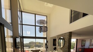 Un salón comedor amplio con ventanas grandes, una pared de piedra decorativa y muebles modernos.