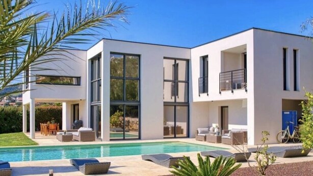 Una casa moderna de dos pisos con piscina, mobiliario exterior y un balcón.