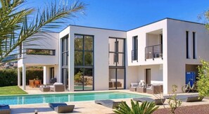 Une maison moderne à deux étages dotée d’une piscine, d’un espace salon extérieur et d’un balcon.