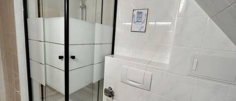 Un baño moderno con ducha acristalada, azulejos blancos y un letrero visible en la pared.