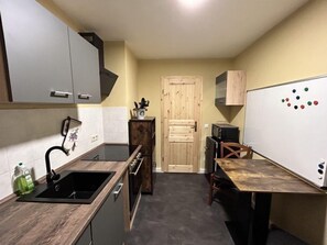 Une cuisine de taille réduite, équipée d’un évier, de placards, d’une porte en bois et d’un tableau blanc orné de points de couleur.