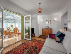 Una sala de estar moderna con un sofá, un televisor, un mueble de madera y una zona de comedor con sillas de mimbre y una mesa.
