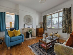 A living room with a blue sofa, a fireplace, a coffee table, and a large window with curtains. - Suilven by Interhome (Drumnadrochit)
