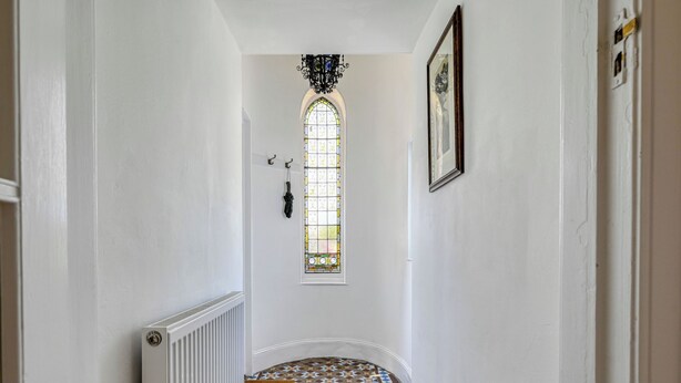 Um corredor com piso estampado, um radiador, uma luminária pendente e uma janela com vitrais.