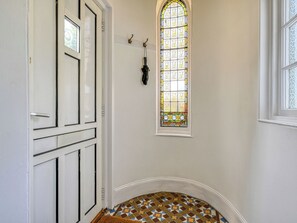 A hallway with a white door, a stained glass window, and a patterned floor.