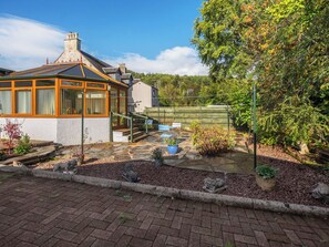A house with a conservatory, a stone pathway, and a garden with plants and a bench.