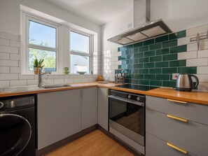A compact kitchen with a built-in dishwasher, oven, and a window with a view of greenery.