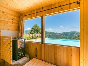 Eine Holzhütte mit Holzboden, einem Fenster mit Blick auf Pool und Berge sowie einer Sauna.