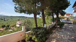 A stone pathway leading to a building with a balcony, surrounded by trees and a view of a hilly landscape.