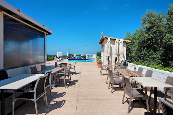 An outdoor patio area with tables and chairs, a pool, and a view of the sky.