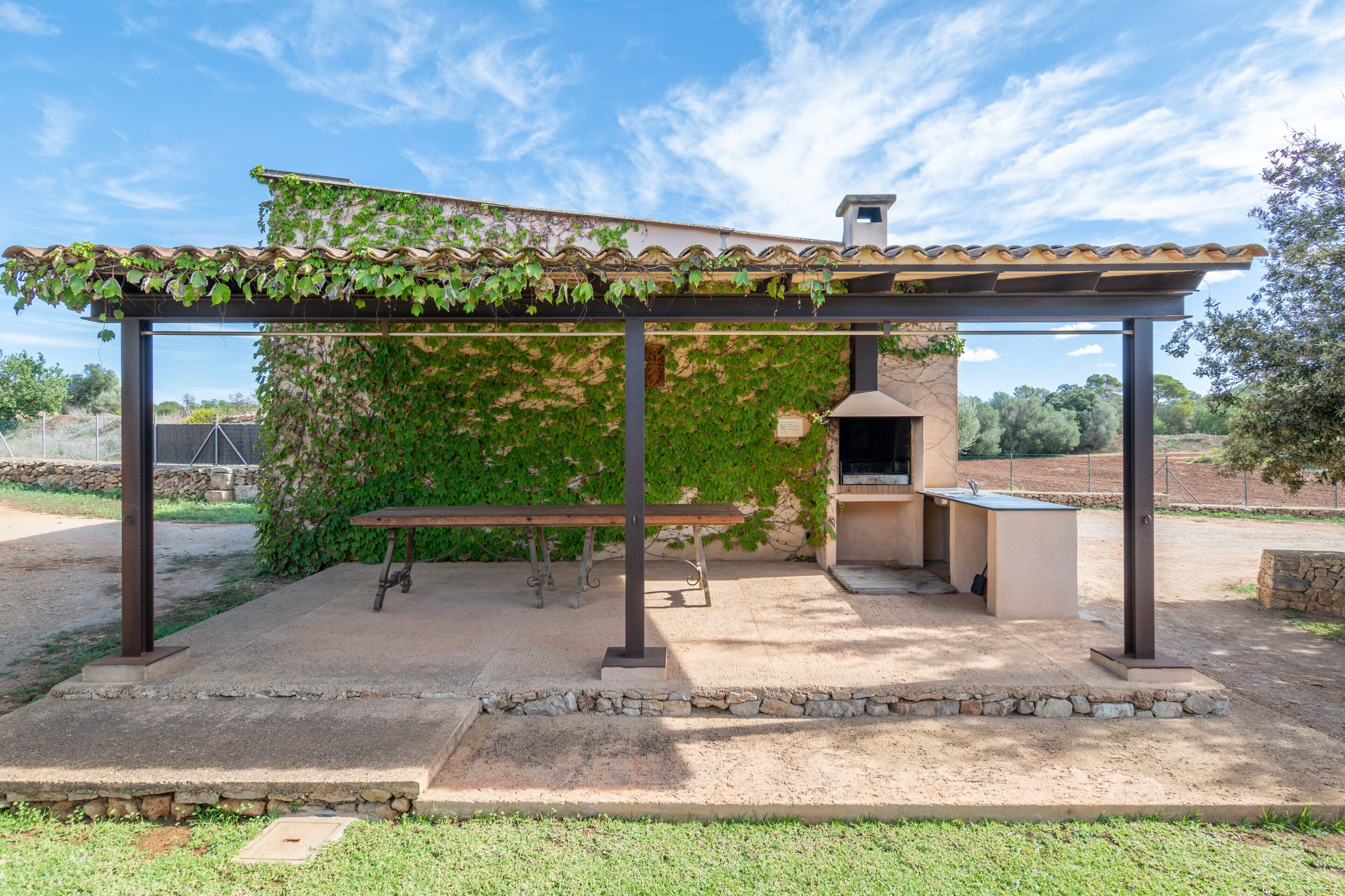 A covered outdoor patio with a grill, a table, and a bench.