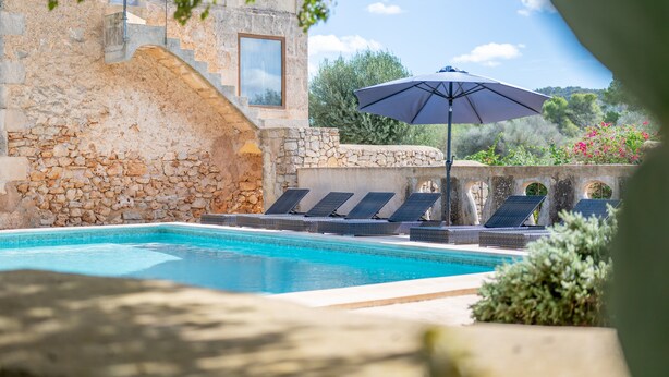 A swimming pool with lounge chairs and an umbrella, stone walls, and a view of the surrounding landscape. - Country House 'Can Menut' with Mountain View, Wi-Fi and Air Conditioning (FELANITX)
