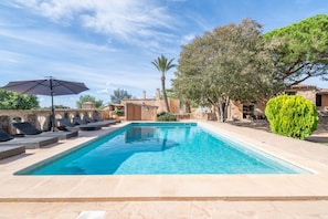 A swimming pool with lounge chairs and an umbrella, surrounded by stone buildings and greenery.