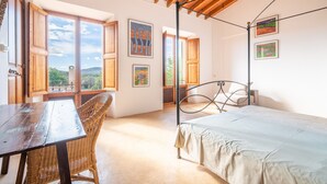 A bedroom with a wooden ceiling, a four-poster bed, a wicker chair, and artwork on the walls. - Country House 'Can Menut' with Mountain View, Wi-Fi and Air Conditioning (FELANITX)