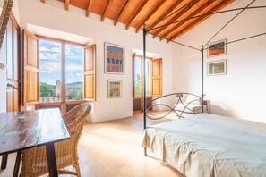 A bedroom with a wooden ceiling, a four-poster bed, a wicker chair, and artwork on the walls. - Country House 'Can Menut' with Mountain View, Wi-Fi and Air Conditioning (FELANITX)