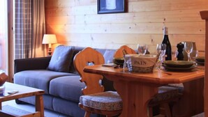 A cozy room with a wooden wall, a framed painting of sunflowers, a dining table set with plates, glasses, and a bottle of wine. - Grand-Hôtel B35 by Interhome (Villars)