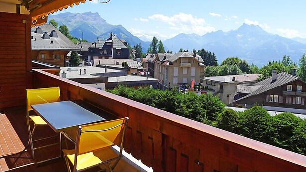 A balcony with a table and chairs, overlooking a town with mountains in the background. - Grand-Hôtel B35 by Interhome (Villars)