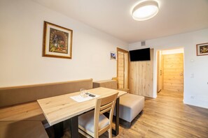 Una habitación con una mesa de comedor de madera, asientos acolchados, un cuadro enmarcado y un televisor en la pared.