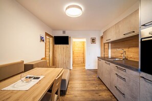 Una cocina compacta con armarios de madera, horno integrado y un banco en la mesa de comedor.