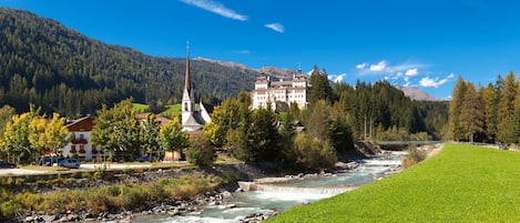Vista a la orilla del río con una iglesia, un edificio grande y una montaña al fondo.