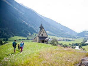 A church with a steep roof and a bell tower, surrounded by a green valley and mountains.
