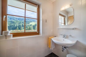 A bathroom with a window, a sink, a mirror, and a towel rack.