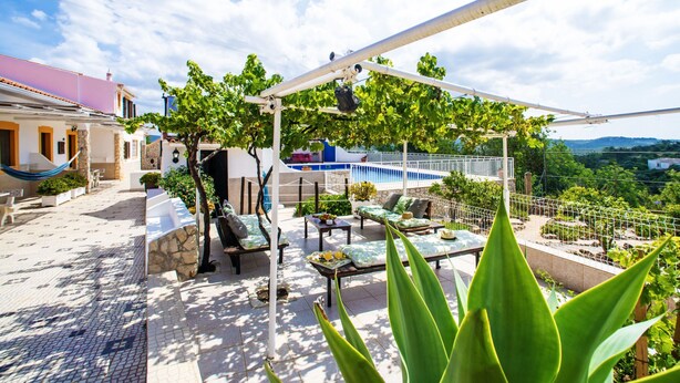 Um terraço no topo do prédio com piscina, área de estar externa e muita vegetação.