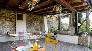 Une terrasse extérieure avec des murs en pierre, des poutres en bois et des tables dressées pour le repas.