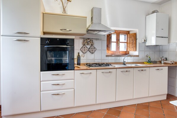 A kitchen with white cabinets, a black oven, a gas stove, a window with wooden shutters, and a tiled backsplash.