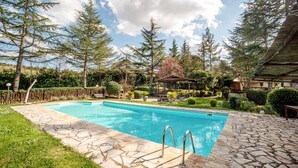 Une piscine rectangulaire revêtue de carreaux de pierre, entourée d’une clôture en bois, d’arbres et d’un belvédère.