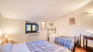 Un dormitorio con dos camas, una ventana, un radiador, una lámpara y un cuadro enmarcado en la pared.