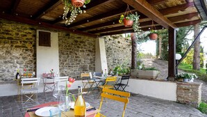 Une terrasse extérieure avec des murs en pierre, des poutres en bois et plusieurs tables et chaises.