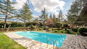 Une piscine rectangulaire revêtue de carreaux de pierre, entourée d’une clôture en bois, d’arbres et d’un belvédère.