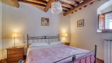 Een slaapkamer met een bed, twee nachtkastjes met lampen, houten balken in het plafond en twee ingekaderde foto's aan de wand.