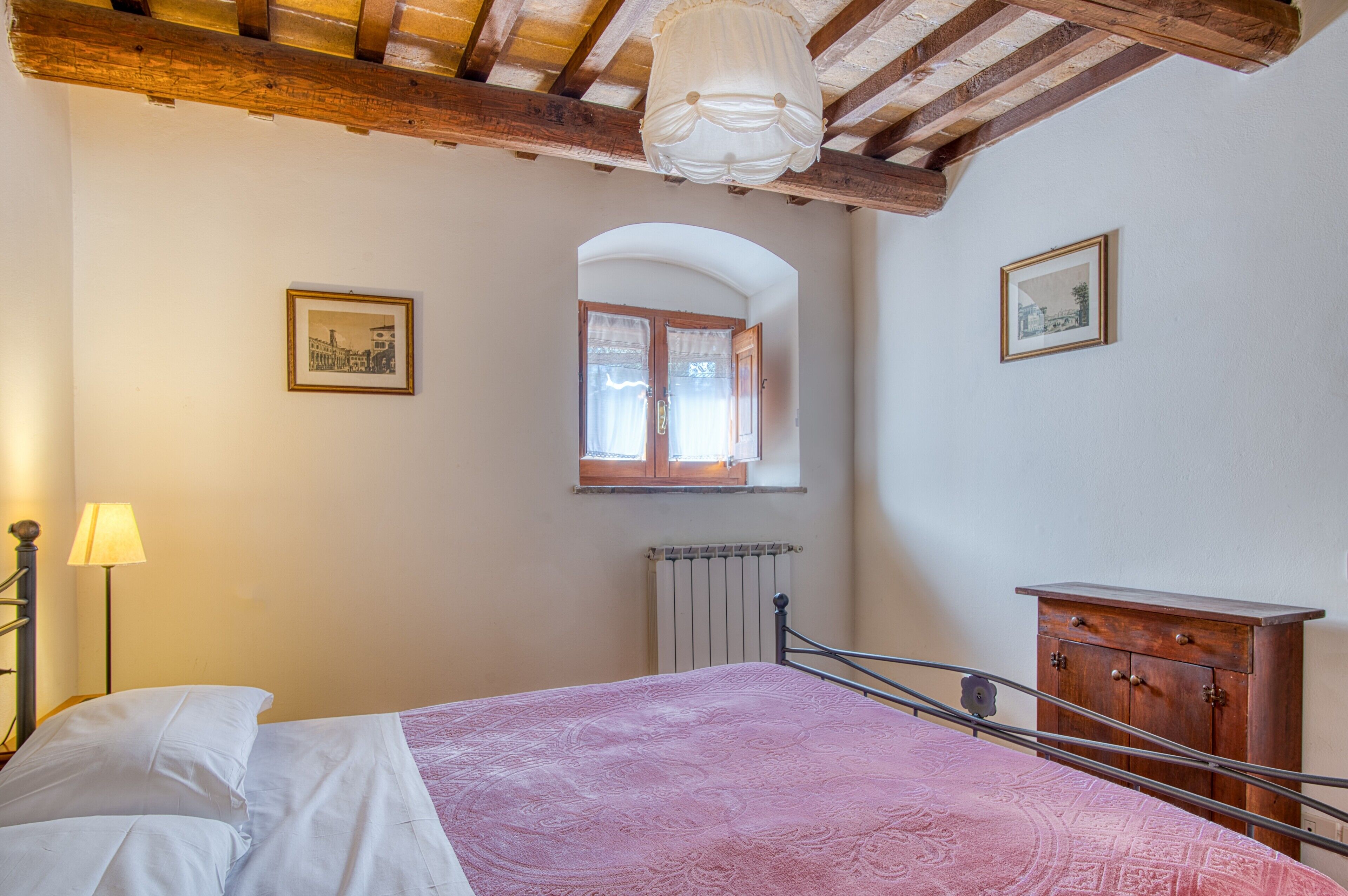 Ein Schlafzimmer mit einem Bett, einem Holzschrank, einem Heizkörper und einem Fenster mit Vorhängen.