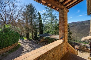A stone wall, a wooden pergola, and a view of a mountainous landscape.
